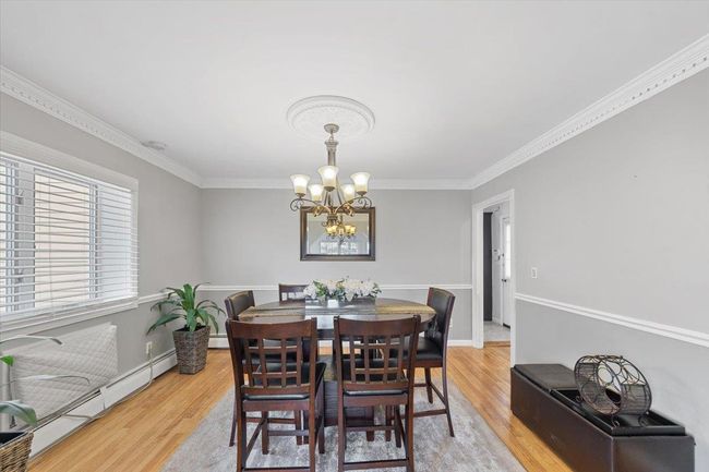 Dining room with light wood finished floors, an inviting chandelier, ornamental molding, and a baseboard radiator | Image 26