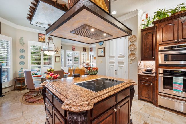 Kitchen featuring black electric stovetop, a warming drawer, ornamental molding, a center island, and light stone countertops | Image 27