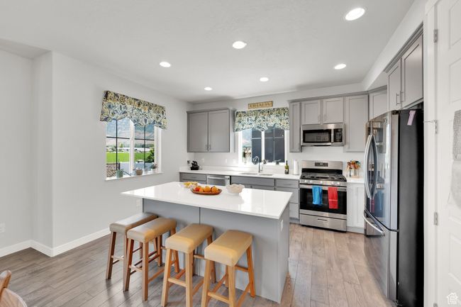 Kitchen with appliances with stainless steel finishes, gray cabinets, a kitchen bar, light wood-style flooring, and recessed lighting | Image 6