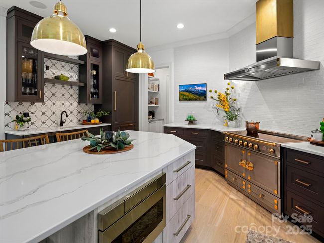 The quartz island features an under counter stainless Sharp microwave oven and easy to access storage drawers. Frame TV is on the far wall above the counter. To the left of the TV is a view of the coffee bar with open shelving. | Image 17