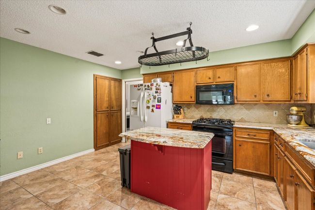Kitchen featuring black appliances, decorative backsplash, a kitchen island, brown cabinetry, and a textured ceiling | Image 14