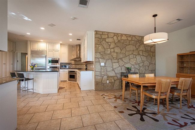 Kitchen featuring built in appliances, wall chimney exhaust hood, tasteful backsplash, dark countertops, and white cabinets | Image 9