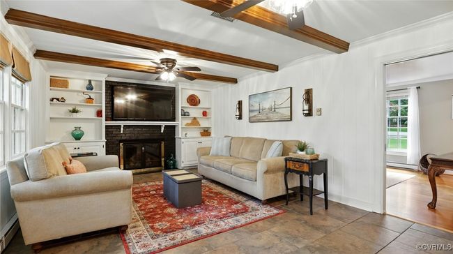 Living room featuring a ceiling fan, crown molding, a brick fireplace, beamed ceiling, and a baseboard heating unit | Image 34
