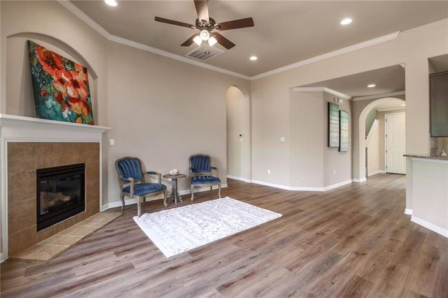 Living area with arched walkways, a tile fireplace, wood finished floors, ceiling fan, and ornamental molding | Image 7