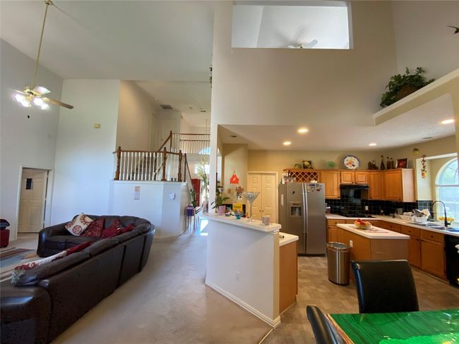 Kitchen featuring decorative backsplash, stainless steel refrigerator with ice dispenser, ceiling fan, a high ceiling, and a center island | Image 16
