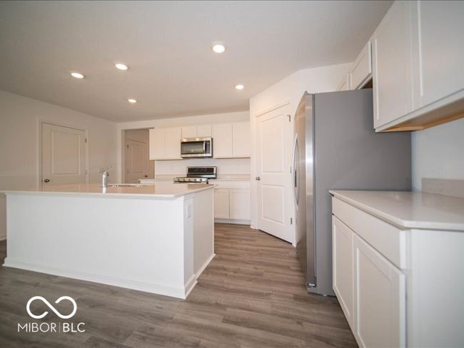 kitchen with a center island with sink, light countertops, appliances with stainless steel finishes, wood finished floors, and white cabinets | Image 20