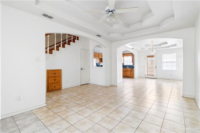 Unfurnished living room featuring a raised ceiling, a ceiling fan, arched walkways, light tile patterned floors, and a chandelier | Image 4