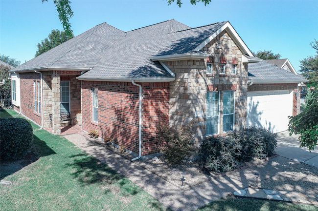 View of side of property with an attached garage, stone siding, roof with shingles, and a yard | Image 4