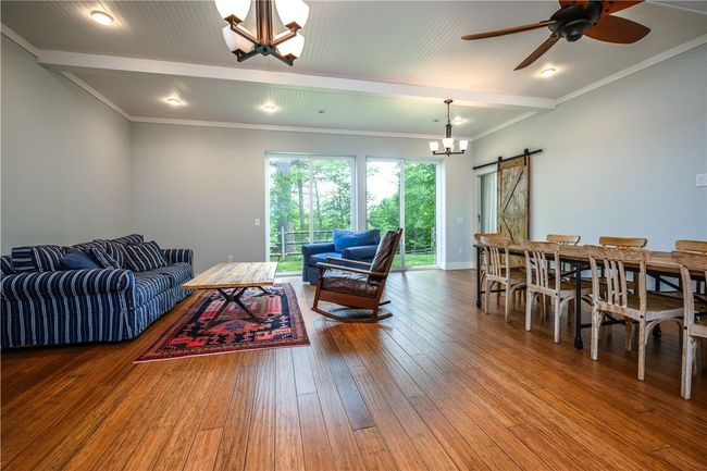 Living room featuring a barn door, beam ceiling, ceiling fan with notable chandelier, and dark wood-type flooring | Image 19