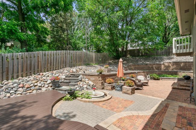 Beautifully landscaped backyard with terraced stonework, a charming water feature, vibrant flowerbeds, and multiple patio areas ideal for outdoor entertaining. | Image 18