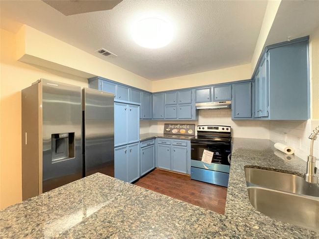 Kitchen featuring appliances with stainless steel finishes, under cabinet range hood, blue cabinetry, dark wood-style flooring, and a textured ceiling | Image 10