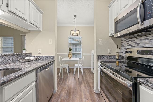 Kitchen featuring stainless steel appliances, dark wood-style floors, ornamental molding, white cabinetry, and backsplash | Image 11