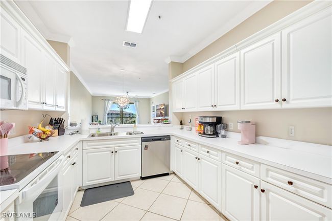 Kitchen with white appliances, sink, white cabinetry, pendant lighting, and crown molding | Image 7