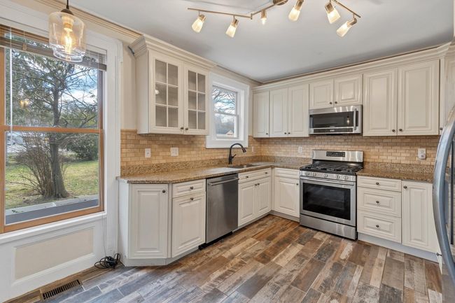 Kitchen featuring stainless steel appliances, a sink, glass insert cabinets, light stone counters, and backsplash | Image 13