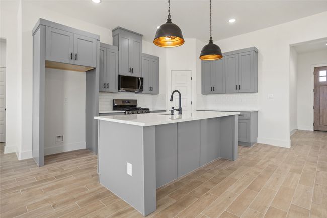 Kitchen with gray cabinetry, a kitchen island with sink, stainless steel appliances, and backsplash | Image 7