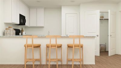 Kitchen featuring a breakfast bar area, light stone countertops, white cabinets, and light hardwood / wood-style floors | Image 2