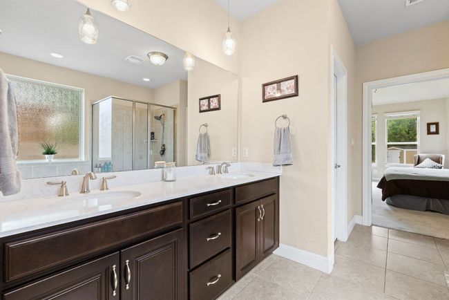Ensuite bathroom featuring double vanity, a shower stall, tile patterned flooring, and baseboards | Image 15