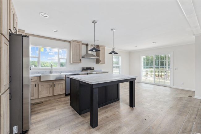 Kitchen with stainless steel appliances, wall chimney exhaust hood, light countertops, crown molding, and light brown cabinets | Image 11