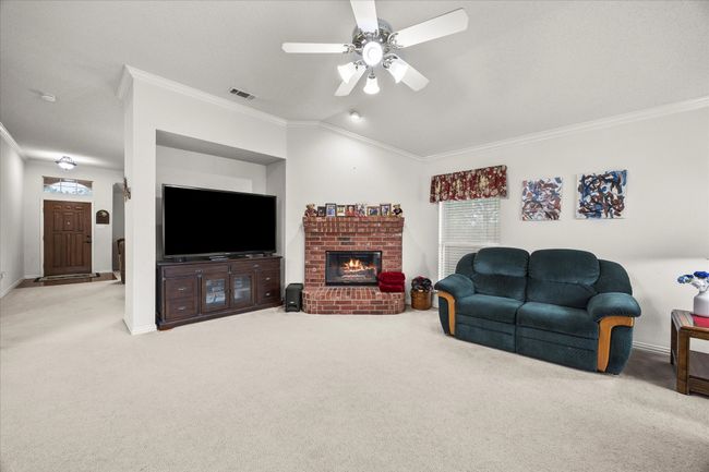 Living area with ornamental molding, carpet flooring, ceiling fan, a brick fireplace, and lofted ceiling | Image 16