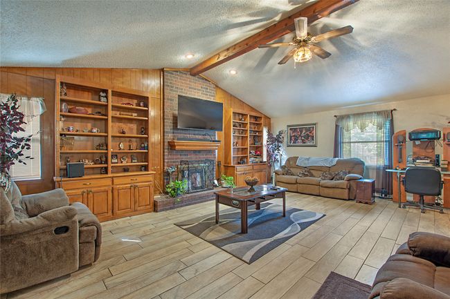 Living room featuring lofted ceiling with beams, a brick fireplace, a textured ceiling, light wood-type flooring, and ceiling fan | Image 4