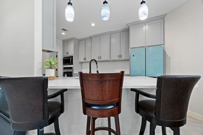 Kitchen with stainless steel appliances, gray cabinets, decorative backsplash, light countertops, and recessed lighting | Image 12