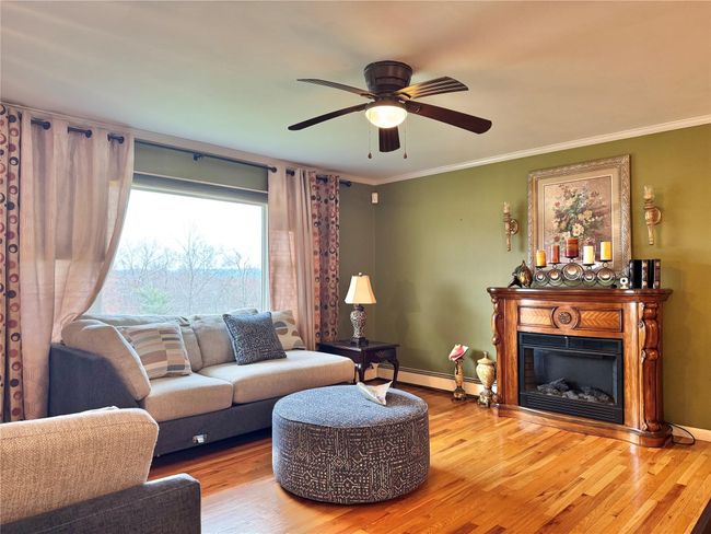 Living area featuring ornamental molding, a glass covered fireplace, a baseboard heating unit, and wood finished floors | Image 5
