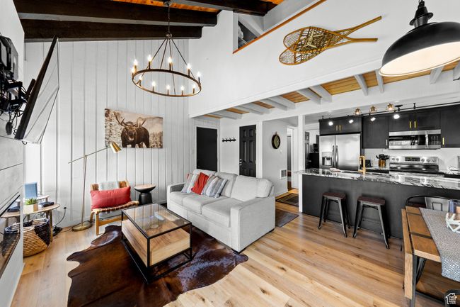 Living area featuring beam ceiling, light wood-style flooring, a chandelier, wooden walls, and a high ceiling | Image 7