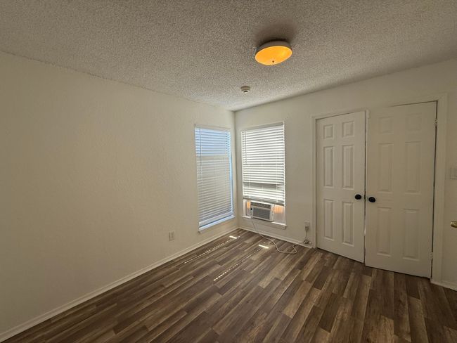 Unfurnished bedroom with a textured ceiling, dark wood-style flooring, cooling unit, and a closet | Image 15
