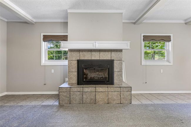Detailed view of a textured ceiling, beamed ceiling, a tiled fireplace, carpet, and baseboards | Image 45