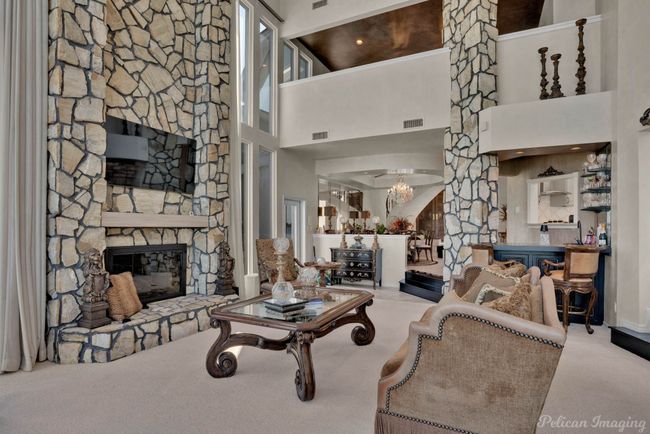 Living area with a notable chandelier, carpet, a stone fireplace, visible vents, and a towering ceiling | Image 11