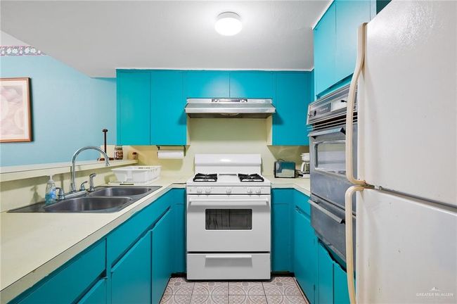 Kitchen with under cabinet range hood, white appliances, light countertops, and a sink | Image 19