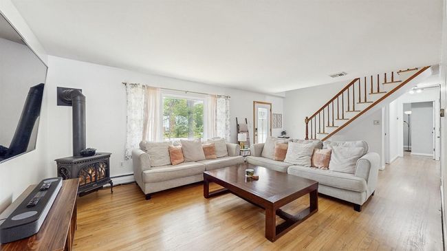 Living room featuring front entry, a gas stove, stairs, light wood finished floors, and baseboard heating. | Image 9
