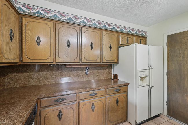 Kitchen featuring white fridge with ice dispenser, dark countertops, brown cabinets, a textured ceiling, and light tile patterned floors | Image 19