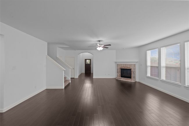 Unfurnished living room with arched walkways, a fireplace, a ceiling fan, stairs, and dark wood-style floors | Image 6