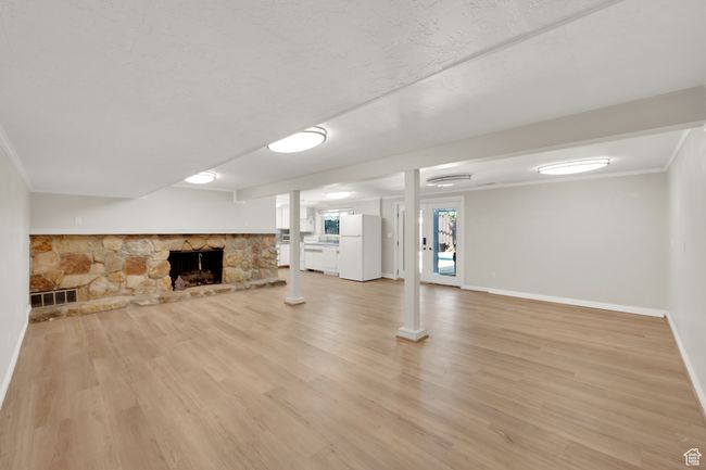 Unfurnished living room featuring light wood-style floors, baseboards, a stone fireplace, and crown molding | Image 26