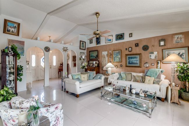 Living room featuring arched walkways, ceiling fan, vaulted ceiling, wooden walls, and light tile patterned flooring | Image 7
