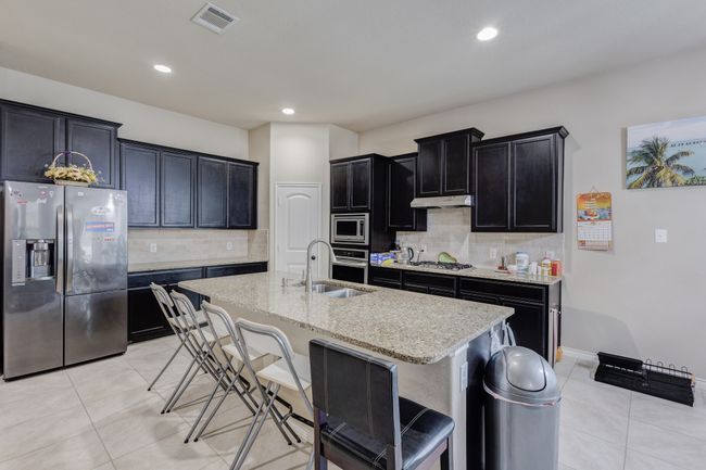 Kitchen featuring stainless steel appliances, a sink, dark cabinets, light tile patterned flooring, and under cabinet range hood | Image 10