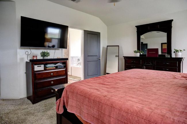 Bedroom with ensuite bathroom, carpet floors, baseboards, lofted ceiling, and visible vents | Image 16