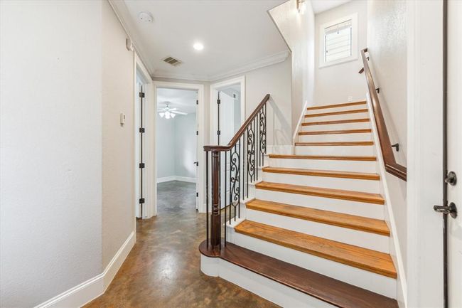A bright entry with polished wooden stairs featuring elegant wrought iron railings. The flooring is a warm, polished concrete, complementing the neutral wall tones. | Image 6