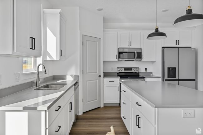 Kitchen featuring decorative light fixtures, a sink, white cabinets, and stainless steel appliances | Image 6