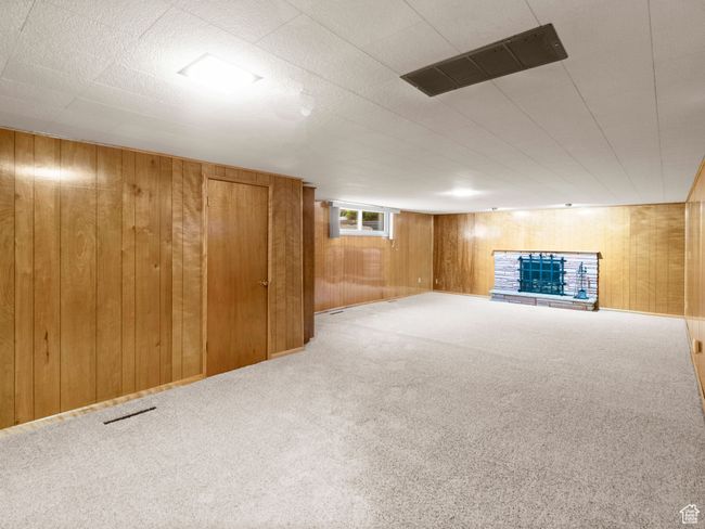 Great room with pristine wood paneling, carpet flooring, and a fireplace with raised hearth | Image 22