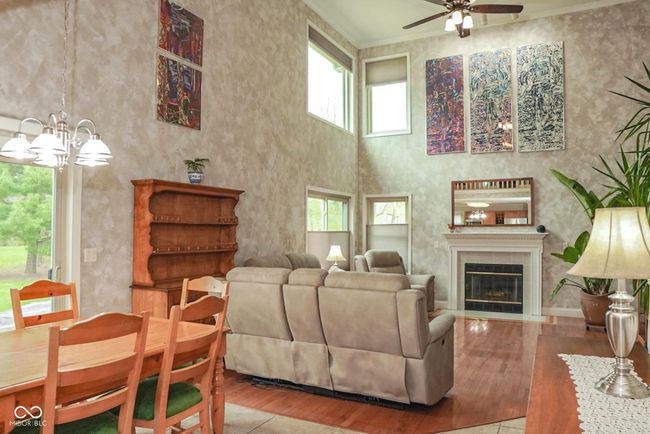 living area with ceiling fan, a high ceiling, wood finished floors, crown molding, and a gas and wood burning fireplace | Image 15