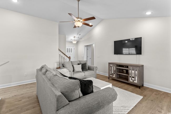 Living room featuring a ceiling fan, vaulted ceiling, baseboards, wood finished floors, and stairs | Image 14