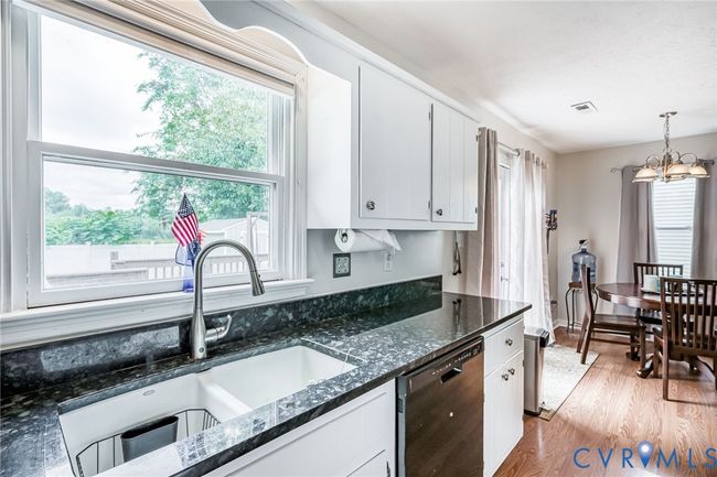 Kitchen featuring a chandelier, light wood-type flooring, white cabinetry, dishwashing machine, and dark stone counters | Image 11