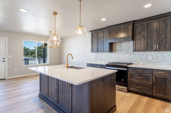 Kitchen with stainless steel stove, light wood-type flooring, tasteful backsplash, light countertops, and a textured ceiling | Image 10