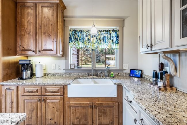 Kitchen featuring light granite counters, hanging pendant light fixtures, w cabinetry, and a farm sink | Image 24