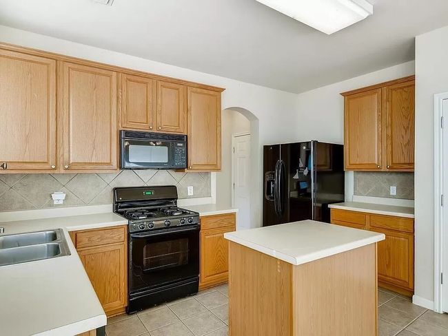 Kitchen with black appliances, light tile patterned floors, arched walkways, and decorative backsplash | Image 10