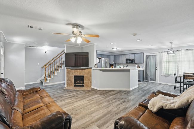 Living room featuring a ceiling fan, ornamental molding, light wood-style flooring, stairs, and a tile fireplace | Image 7