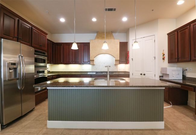 Kitchen with pendant lighting, visible vents, dark stone countertops, a sink, and stainless steel fridge | Image 10