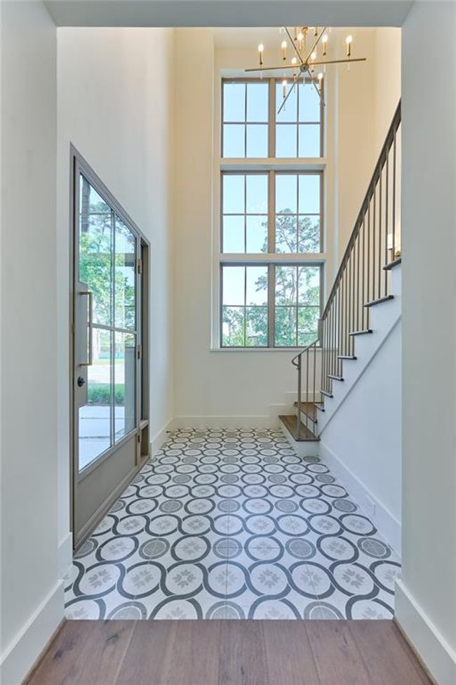 This entryway features a high ceiling with large windows, patterned tile flooring, and a modern chandelier. | Image 4
